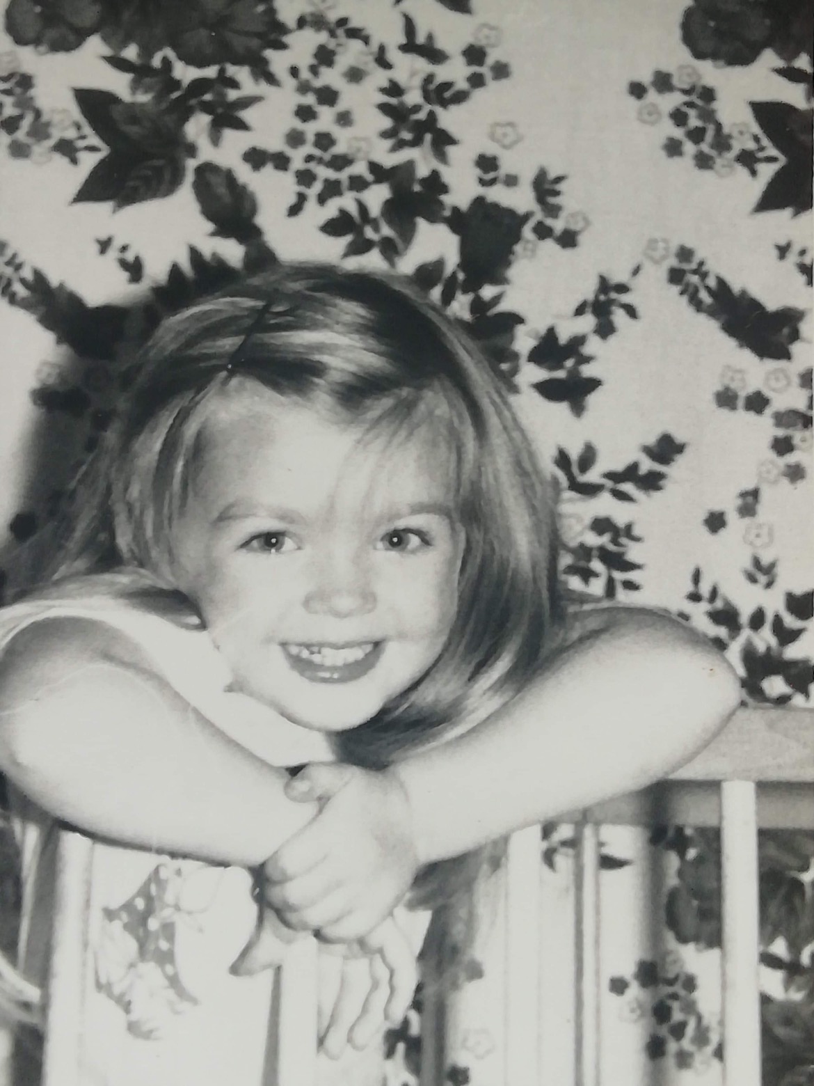 Black-and-white childhood photograph of Eline Mets smiling with her arms resting on a chair