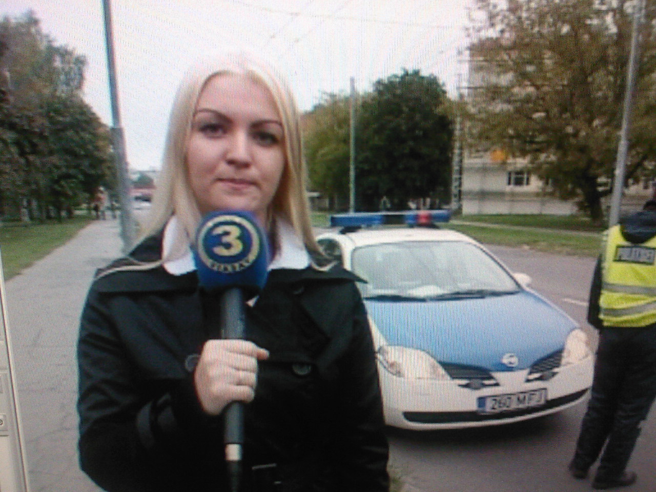 Eline Mets reporting for TV3 Raport beside a police vehicle